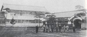 旭学校校舎前の運動場に複数の人が並んで立っている様子の白黒写真
