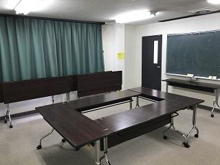 部屋の真ん中に机が4つ輪になるように置かれ、壁には黒板がある会議スペースのような洋室の写真
