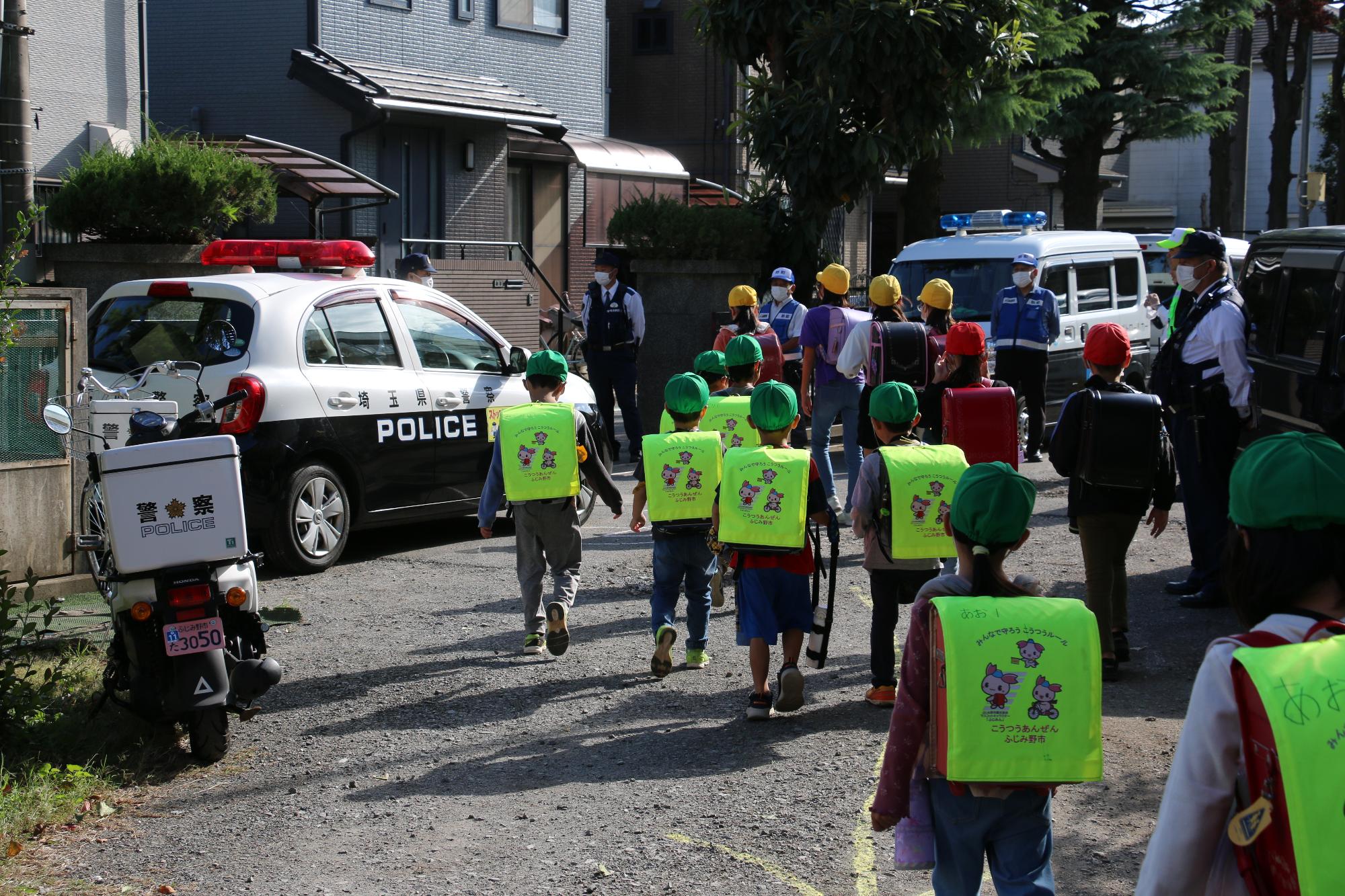 西小学校で警察官と青色防犯パトカー市民パトロール隊が下校する児童を見守る様子の写真